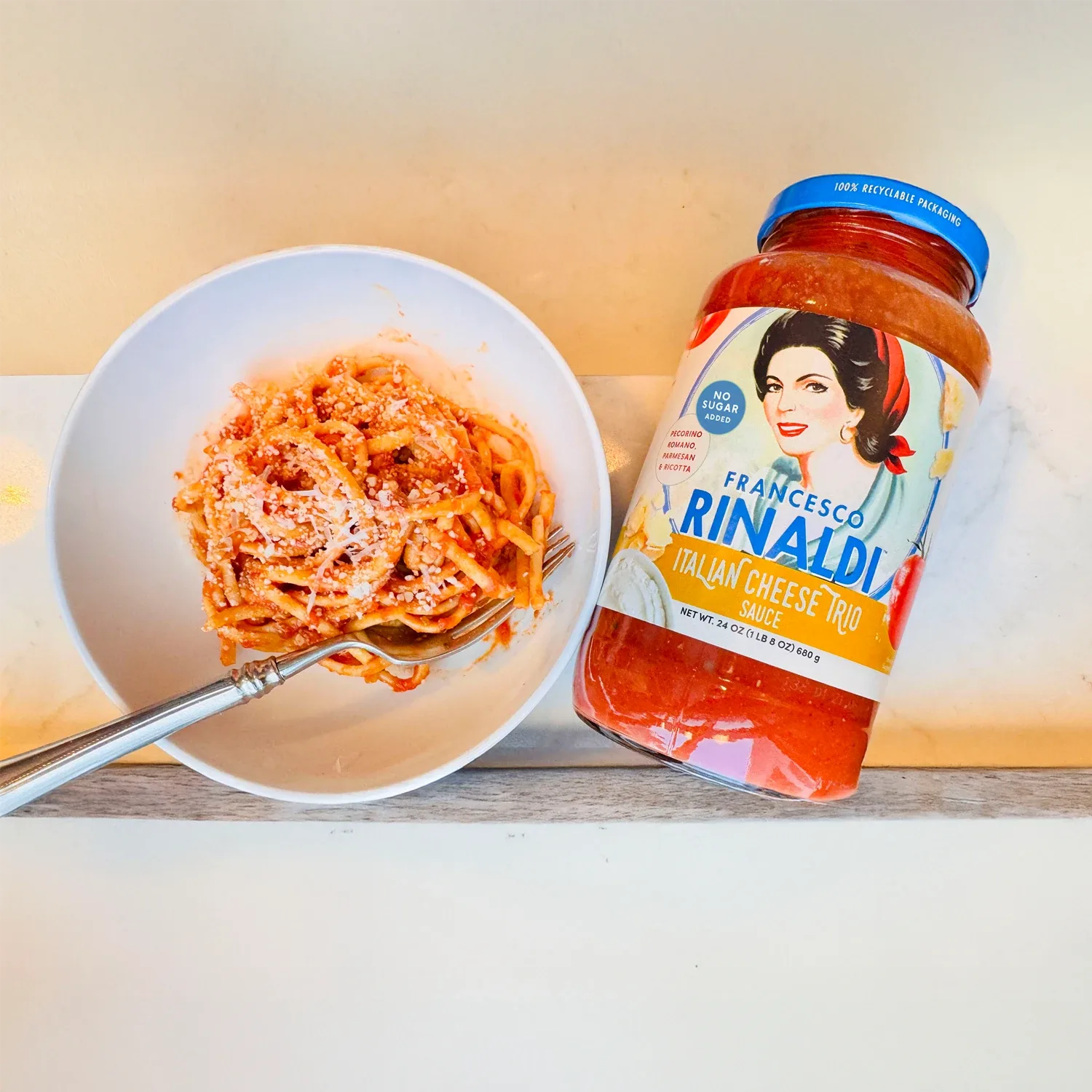 Jar of Francesco Rinaldi Italian Cheese Trio Sauce overhead with a bowl of spaghetti.