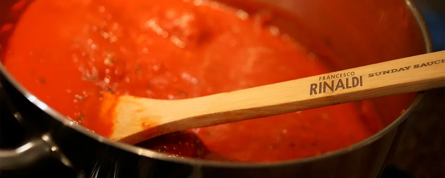 Francesco Rinaldi wooden spoon stirs sauce.
