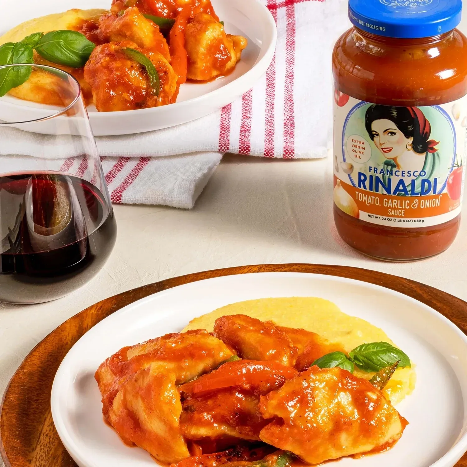 Dish of chicken cacciatore next to a glass of wine and jar of red sauce.