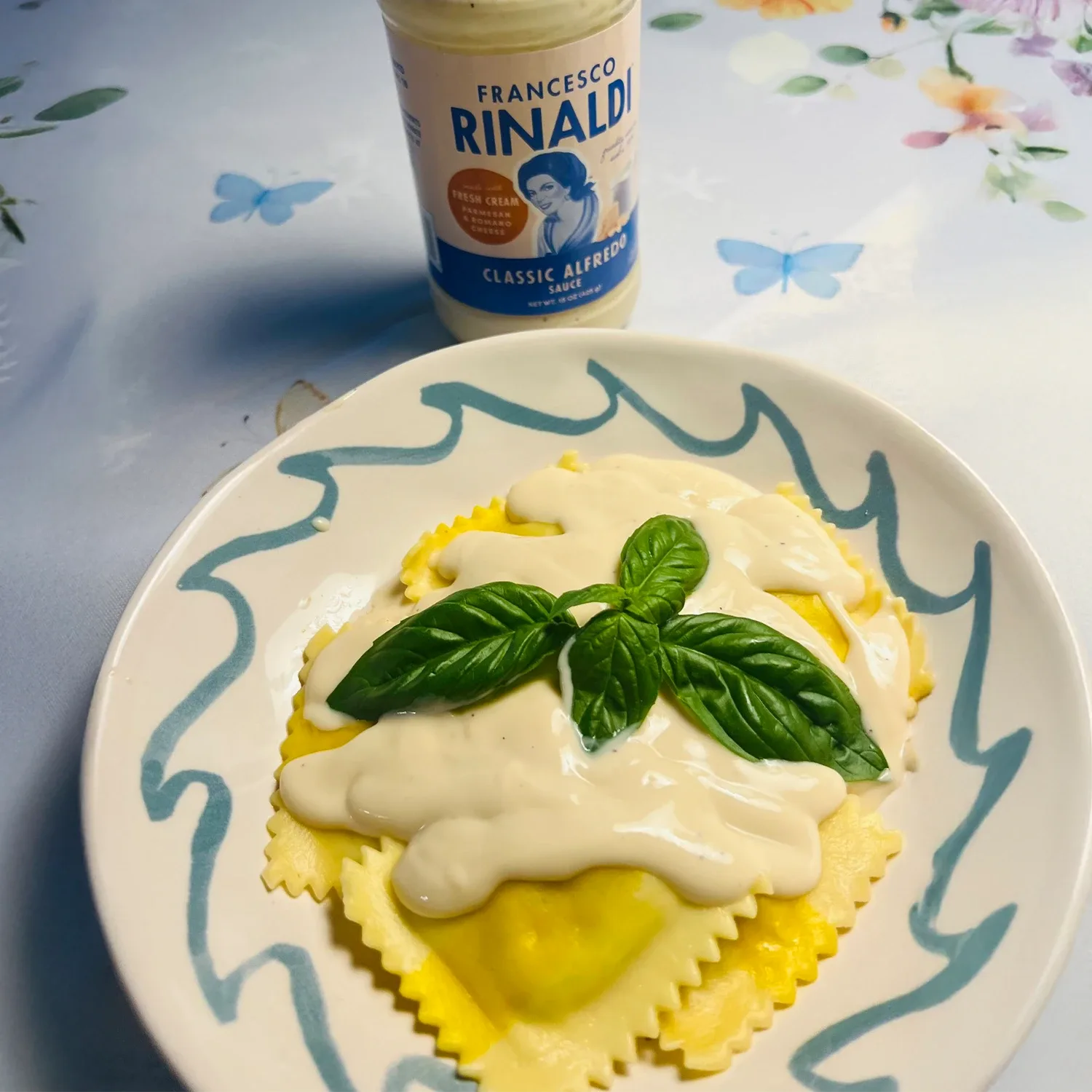 Ravioli in a bowl with sauce next to a jar of Francesco Rinaldi Alfredo sauce.